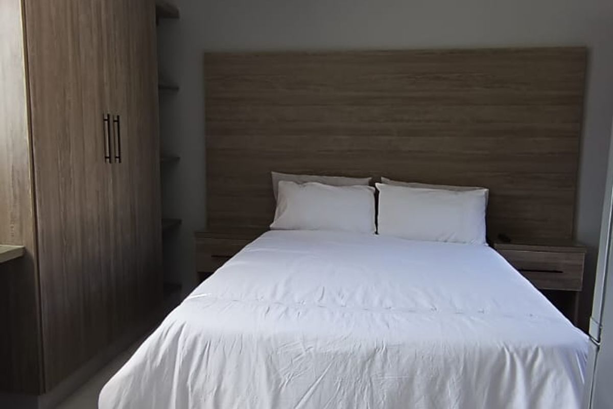 A well-maintained bedroom featuring built-in wooden cabinetry, a matching headboard with integrated bedside tables, and neutral tiled flooring.