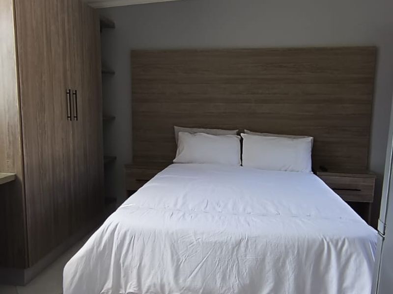 A well-maintained bedroom featuring built-in wooden cabinetry, a matching headboard with integrated bedside tables, and neutral tiled flooring.
