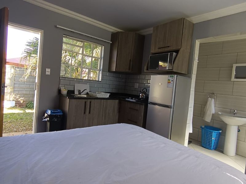 Open-plan studio apartment featuring a compact kitchenette with built-in cabinetry and an adjacent bathroom with a pedestal basin.
