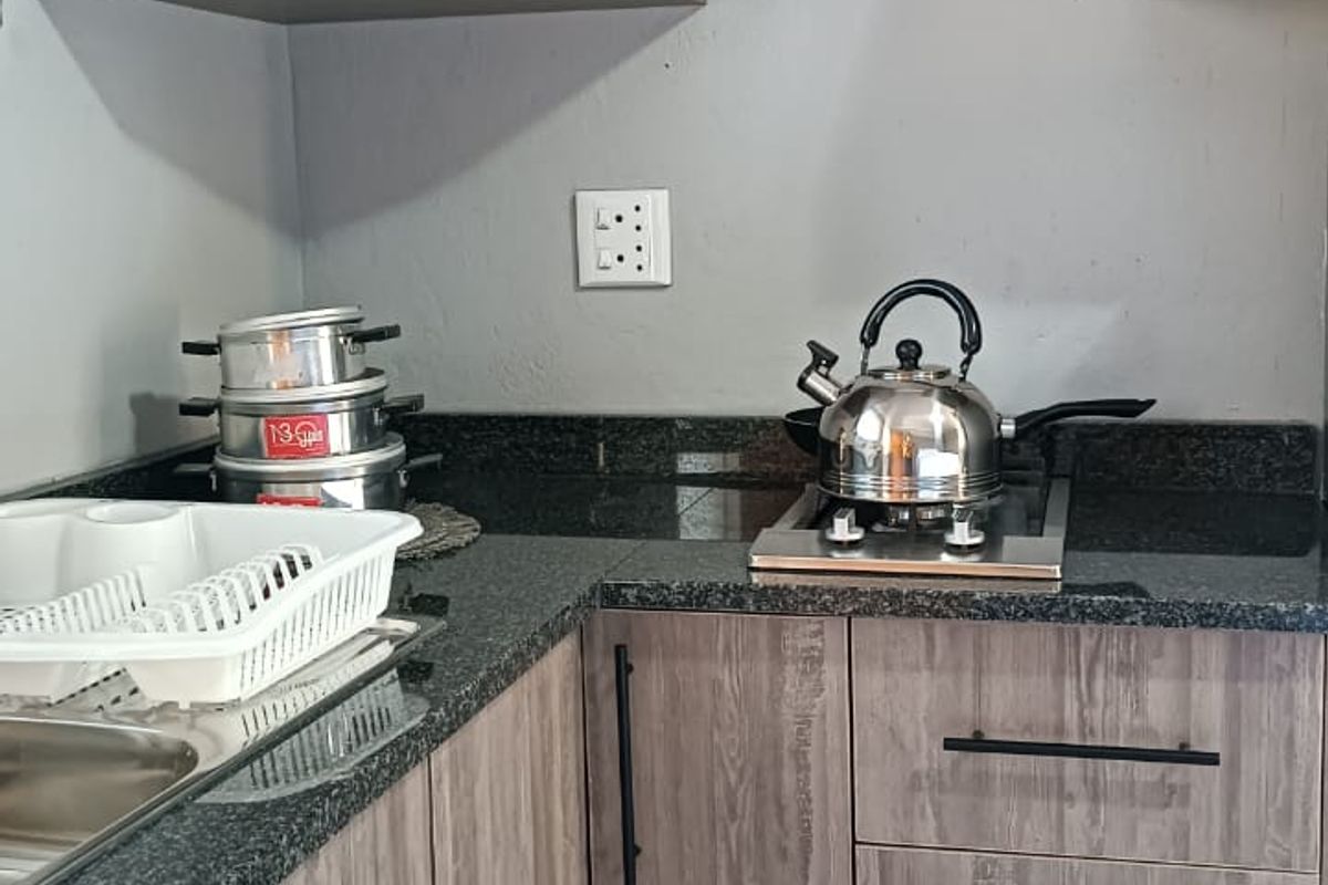 A compact kitchen featuring modern wood-look laminate cabinetry, dark granite countertops, and a built-in hob, providing a functional and efficient workspace.