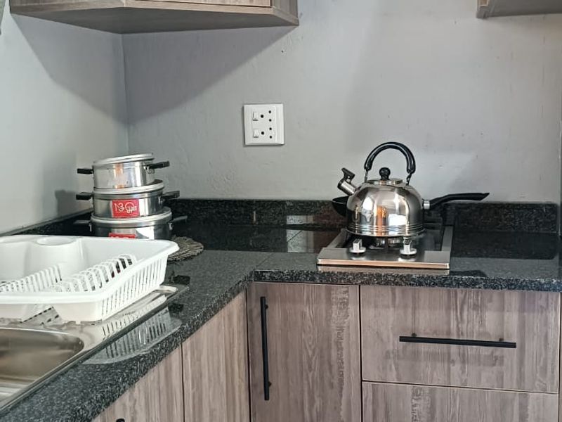 A compact kitchen featuring modern wood-look laminate cabinetry, dark granite countertops, and a built-in hob, providing a functional and efficient workspace.
