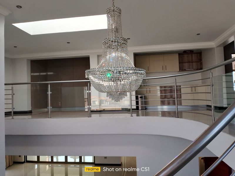 Spacious landing area featuring a grand crystal chandelier, modern stainless steel and glass balustrade, and a skylight providing natural light.