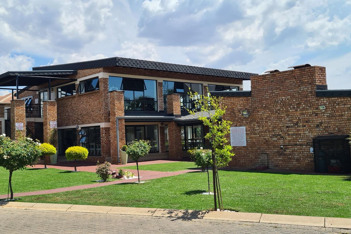 A well-maintained double-story face brick building featuring large windows, a paved walkway, and a manicured garden area.