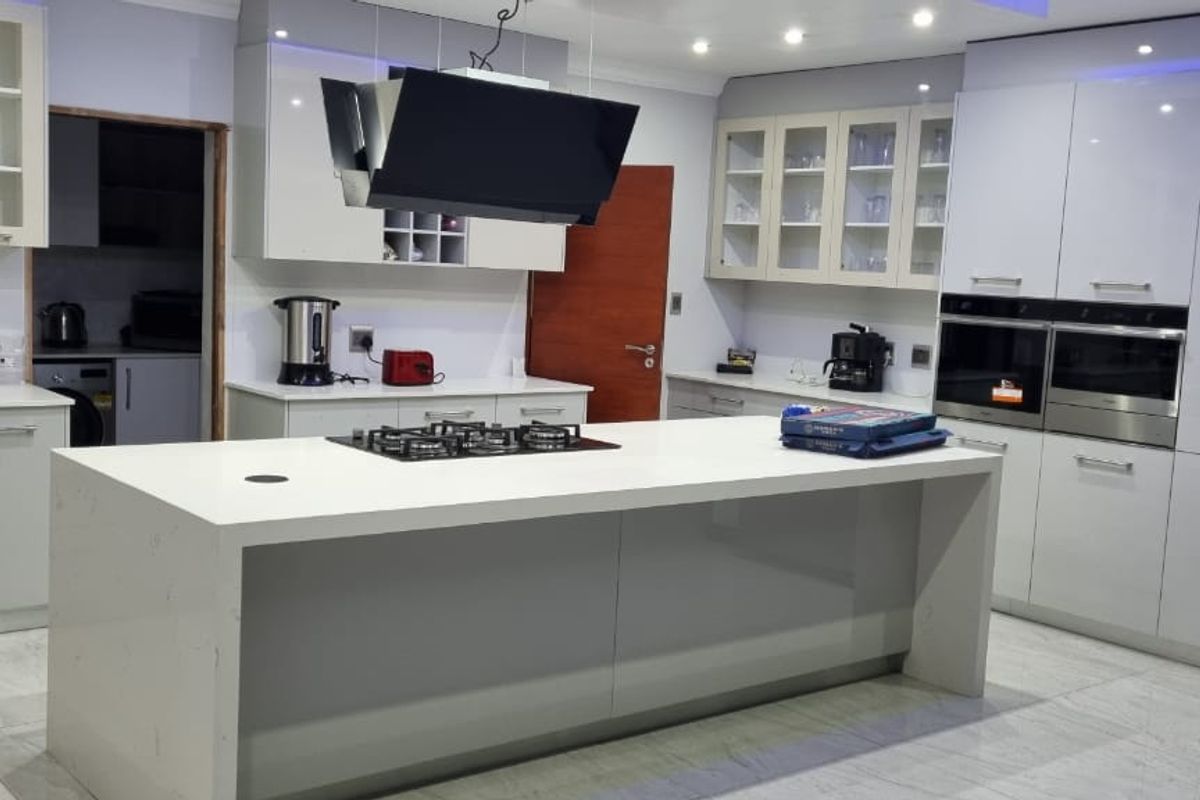 Modern kitchen featuring a large central island with gas hob, high-gloss cabinetry, integrated double ovens, and premium quartz countertops with tiled flooring.