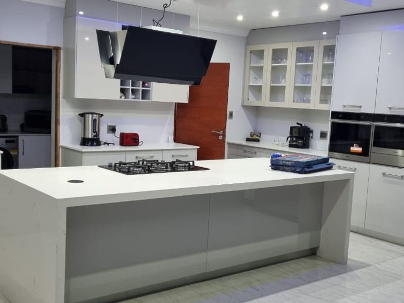 Modern kitchen featuring a large central island with gas hob, high-gloss cabinetry, integrated double ovens, and premium quartz countertops with tiled flooring.