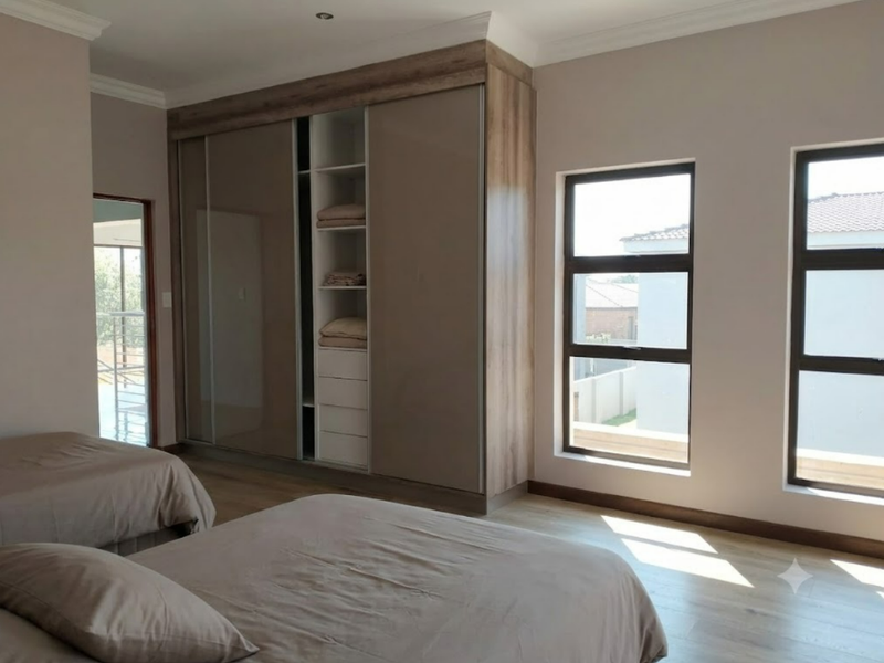 A well-maintained bedroom featuring modern built-in cupboards, laminate flooring, and large windows that provide ample natural light.