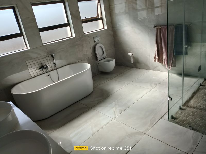 Modern bathroom featuring a freestanding bathtub, wall-mounted toilet, glass-enclosed shower, and double vanity with large format wall and floor tiles.