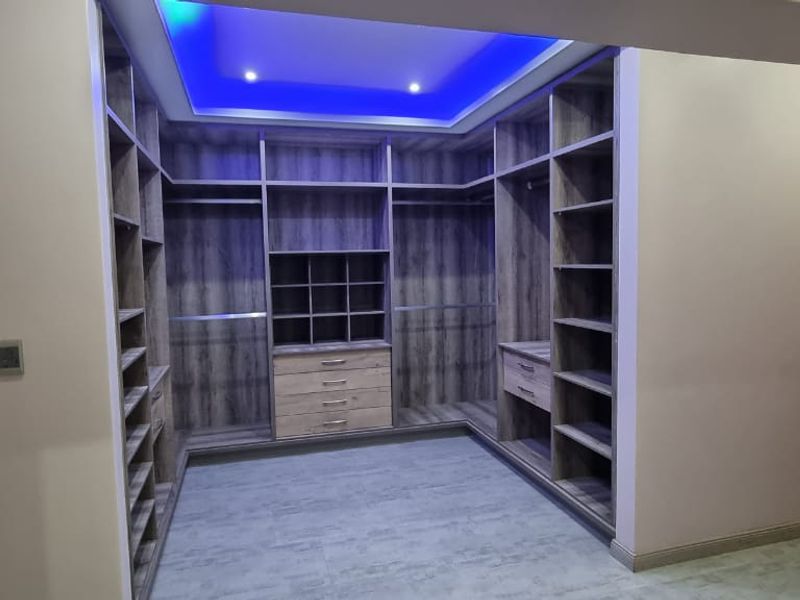 A spacious walk-in closet featuring extensive custom built-in cabinetry, modern tiled flooring, and ambient recessed ceiling lighting.