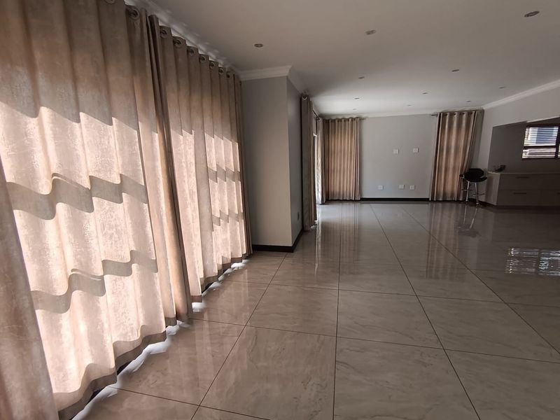 Spacious open-plan living area featuring large format polished floor tiles, recessed downlighting, and neutral wall finishes, offering a bright and versatile living space.