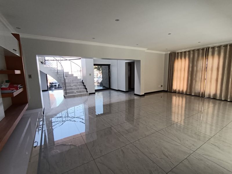 Spacious open-plan living area featuring polished porcelain floor tiles, recessed lighting, and a modern staircase with a metal balustrade.