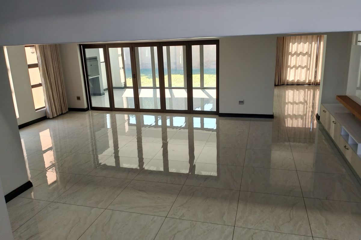 Spacious open-plan living area featuring large format polished floor tiles, modern aluminium stacker doors leading to the garden, and built-in cabinetry.