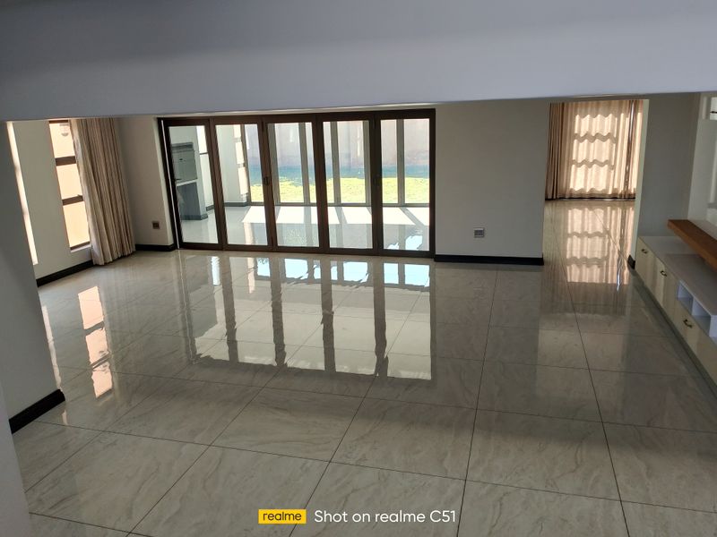 Spacious open-plan living area featuring large format polished floor tiles, modern aluminium stacker doors leading to the garden, and built-in cabinetry.