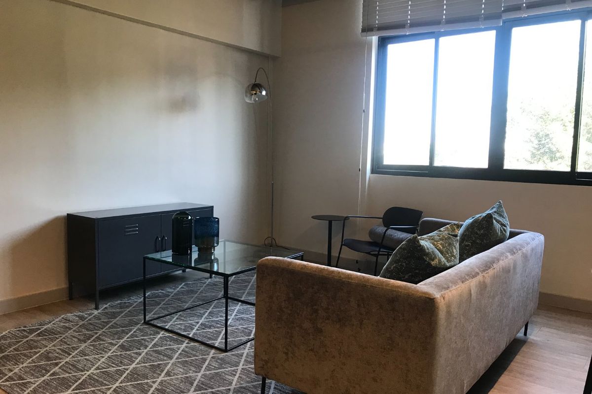 A well-lit living room featuring an exposed ceiling beam, large window with venetian blinds, and neutral wall finishes.