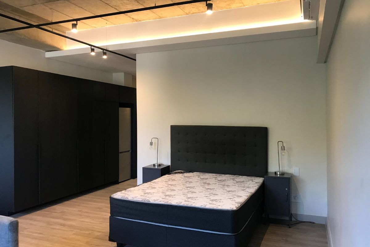 Modern bedroom featuring an exposed concrete ceiling, track lighting, built-in storage cabinetry, and an integrated air conditioning unit.
