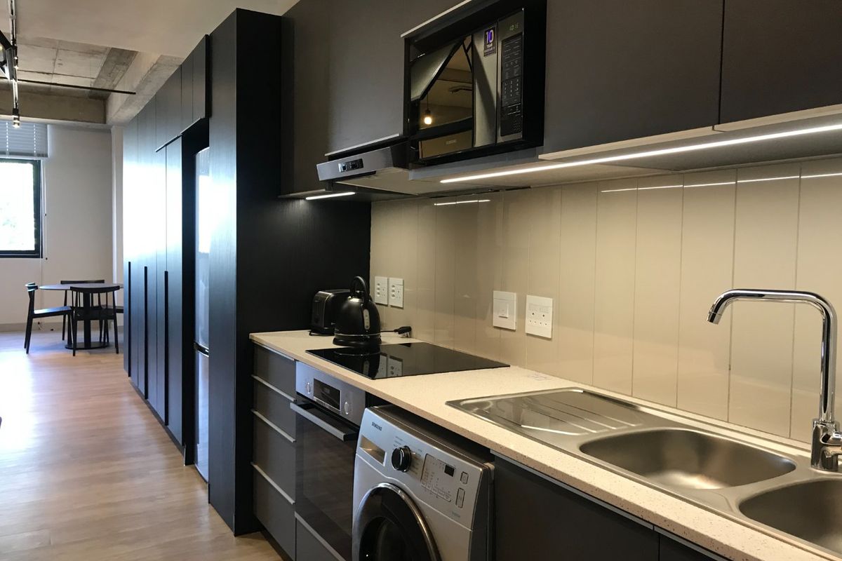 Modern kitchen featuring dark cabinetry, stone countertops, integrated appliances, and a sleek glass splashback, complemented by an industrial-style exposed concrete ceiling.