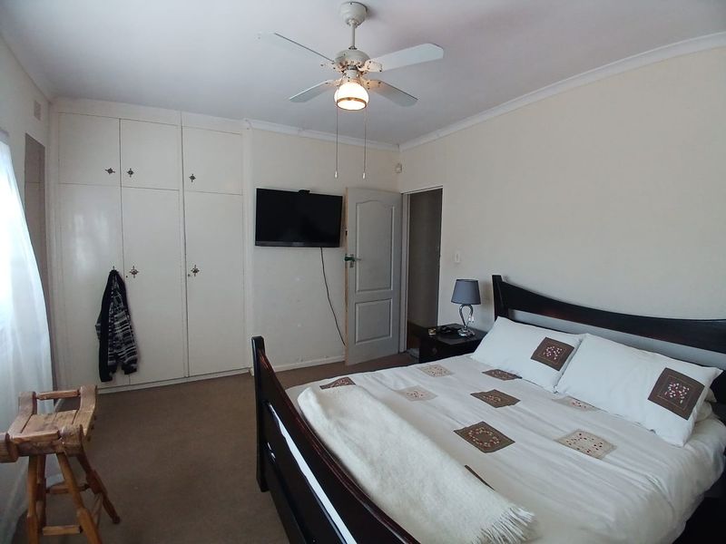 A functional bedroom featuring built-in cupboards, a ceiling fan, and carpeted flooring, offering a neutral space ready for personalization.