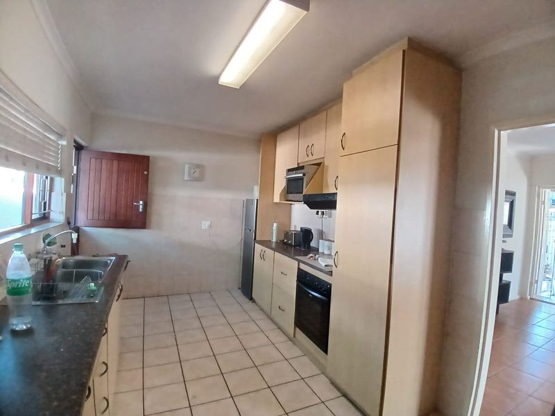 A functional kitchen featuring built-in cabinetry, laminate countertops, a stainless steel sink, and integrated oven with extractor fan, finished with tiled flooring.