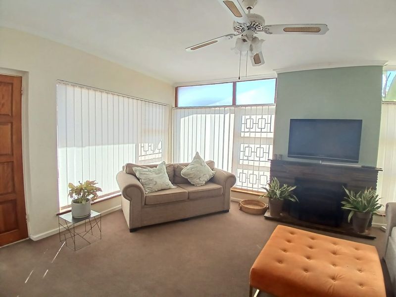 A comfortable living room featuring a fireplace, ceiling fan, and large windows with vertical blinds, providing a bright and functional space.