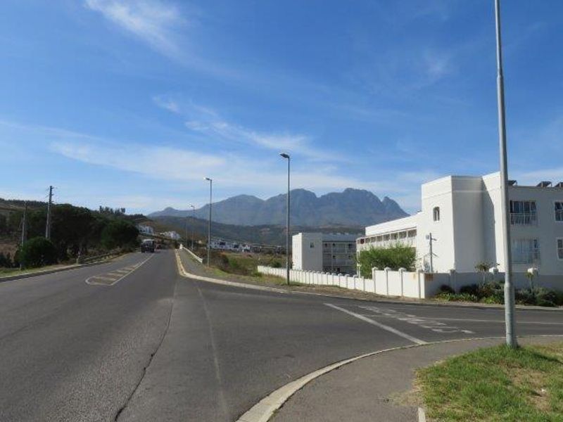A street view showing the local road infrastructure, sidewalk, and surrounding neighbourhood context with mountain views in the distance.