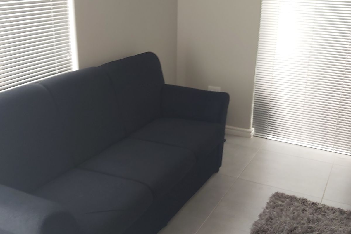 A living room area featuring neutral tiled flooring and fitted venetian blinds on the windows.