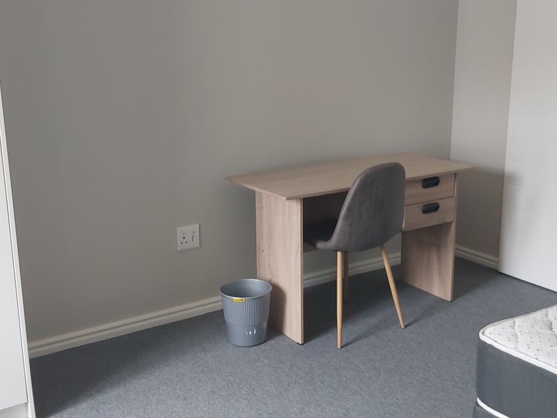 A clean bedroom featuring neutral grey walls, carpeted flooring, and a built-in wardrobe, offering a simple and functional living space.