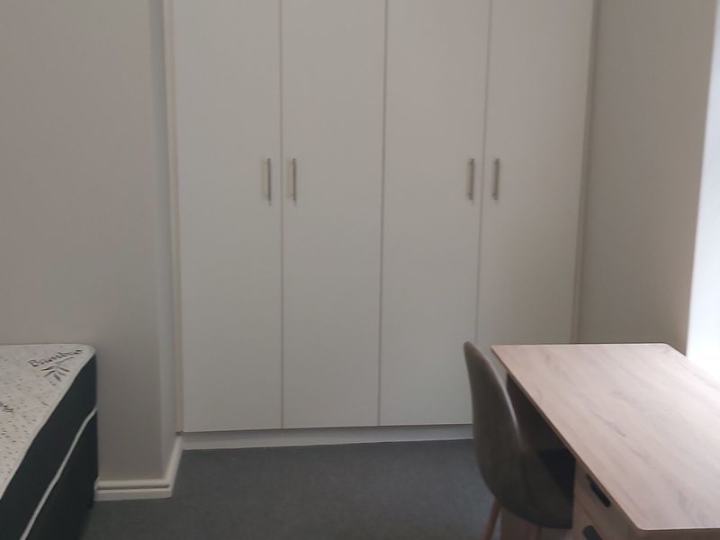 A clean bedroom featuring neutral walls, carpeted flooring, built-in cupboards for storage, and venetian blinds on the window.