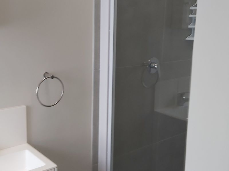 A clean, modern bathroom featuring a vanity basin with mixer tap, wall-mounted mirror cabinet, and a separate shower enclosure with tiled walls.