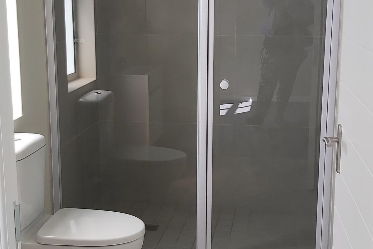 A clean, modern bathroom featuring a glass-enclosed shower, neutral floor-to-ceiling tiling, and a standard white toilet.