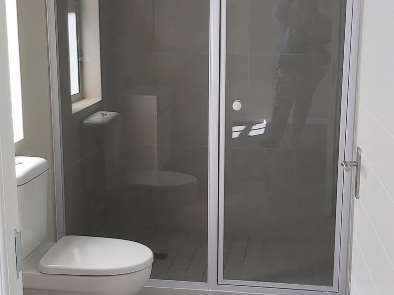 A clean, modern bathroom featuring a glass-enclosed shower, neutral floor-to-ceiling tiling, and a standard white toilet.