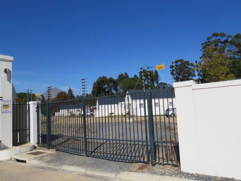 A secure front entrance featuring a metal gate, perimeter walling with electric fencing, and a gravel driveway leading to the property.