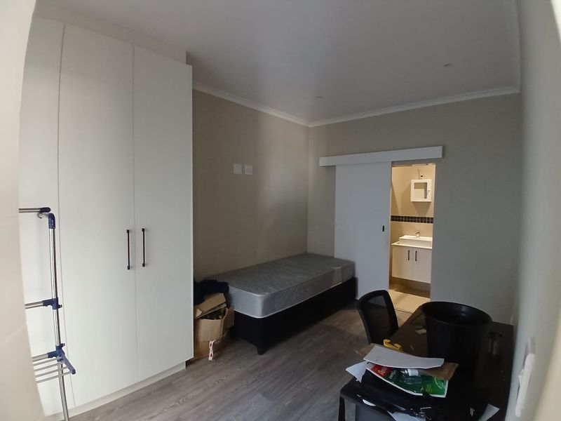 A bedroom featuring built-in wardrobes, laminate flooring, and an en-suite bathroom with a sliding door entrance.