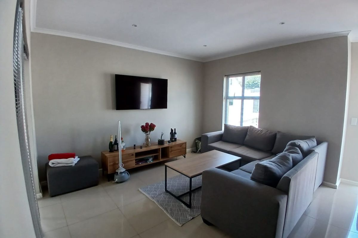 A well-maintained living room featuring neutral wall tones, tiled flooring, recessed downlighting, and a wall-mounted television.
