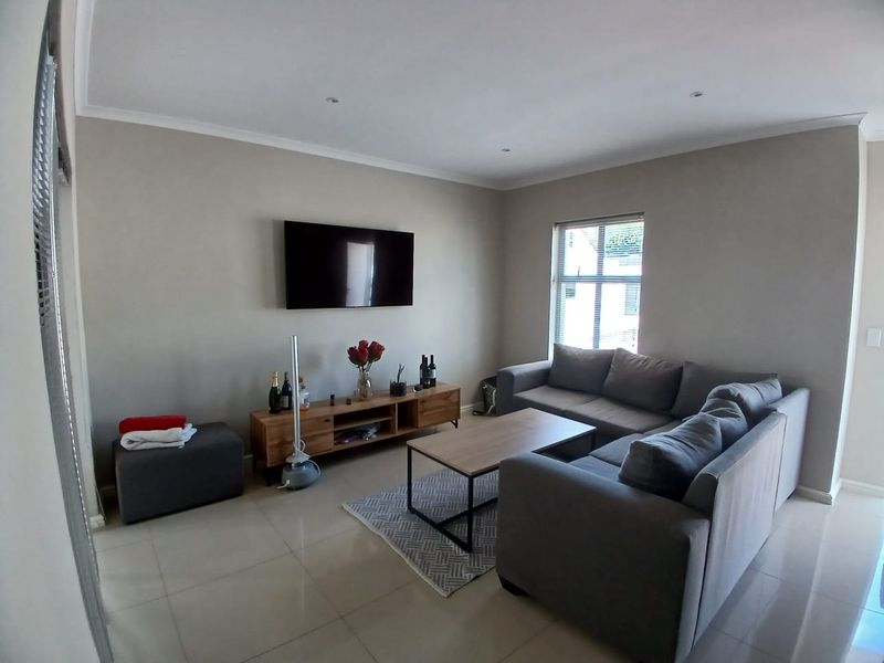 A well-maintained living room featuring neutral wall tones, tiled flooring, recessed downlighting, and a wall-mounted television.
