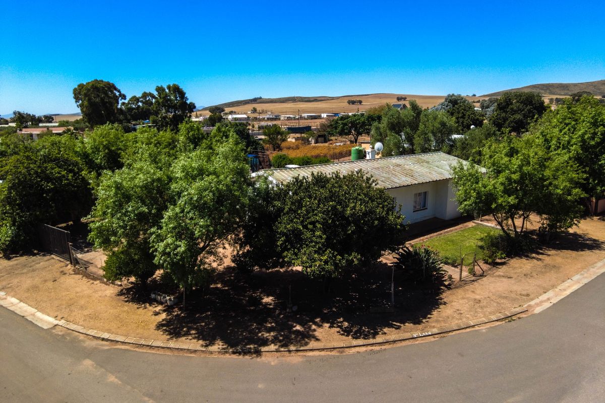 Aerial view of a small holding property featuring a dwelling with a corrugated metal roof, mature trees, and surrounding landscape.
