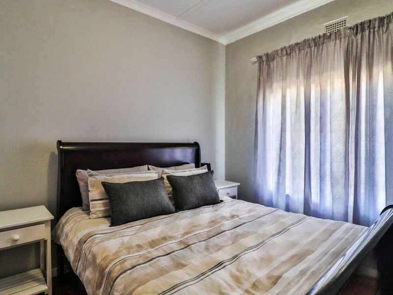 A well-maintained bedroom featuring neutral wall tones, cove cornicing, and a window with fitted curtain tracks.