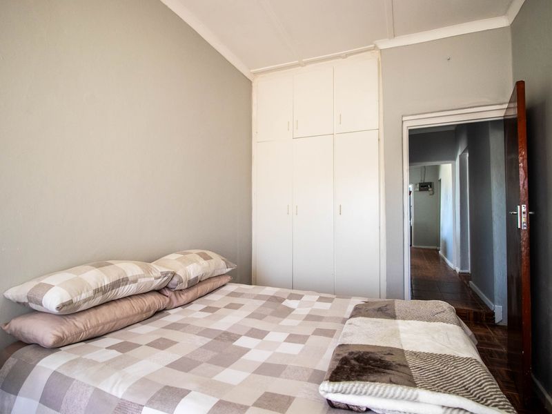 A functional bedroom featuring built-in cupboards, classic wooden parquet flooring, and neutral wall tones, offering a comfortable and practical living space.