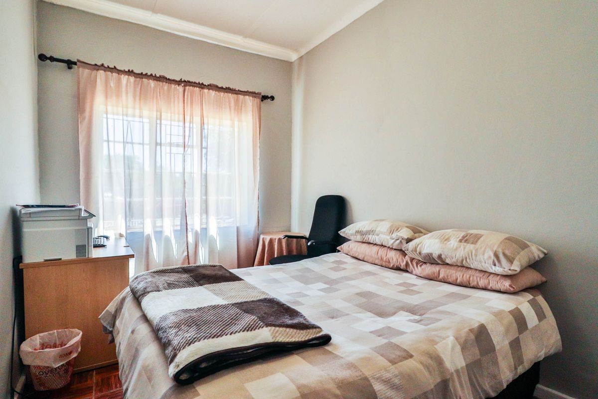 A functional bedroom featuring neutral wall finishes, a window with security bars, and decorative ceiling cornicing.