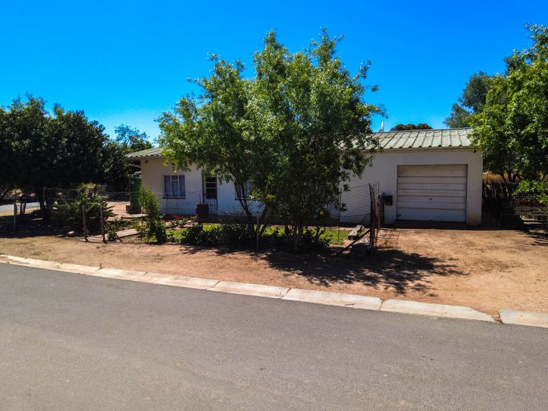 Front view of a single-story small holding property featuring a metal roof, attached garage, and surrounding garden area.