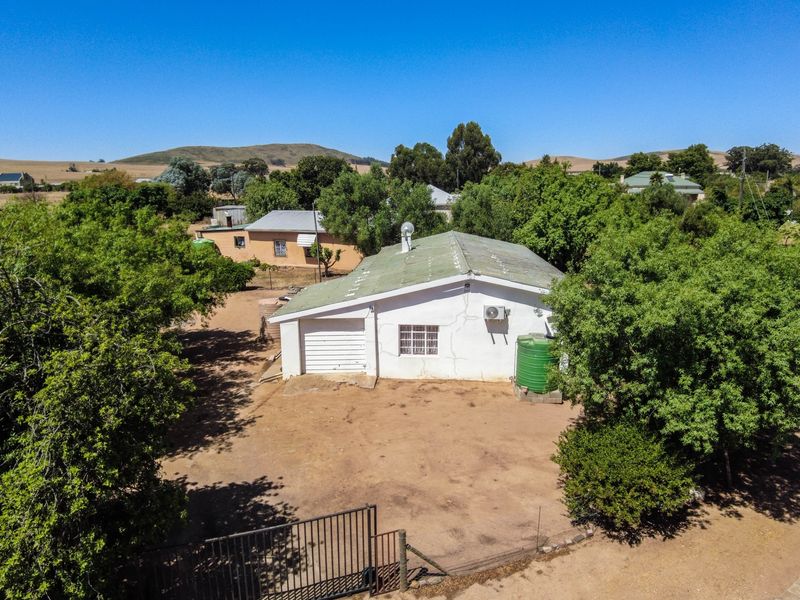 Aerial view of a small holding property featuring a detached structure with a garage, water tank, and surrounding mature trees.