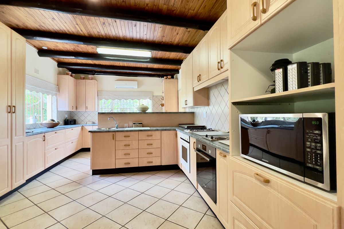 Spacious kitchen featuring light wood cabinetry, tiled countertops, built-in oven and hob, and a distinctive exposed timber beam ceiling.