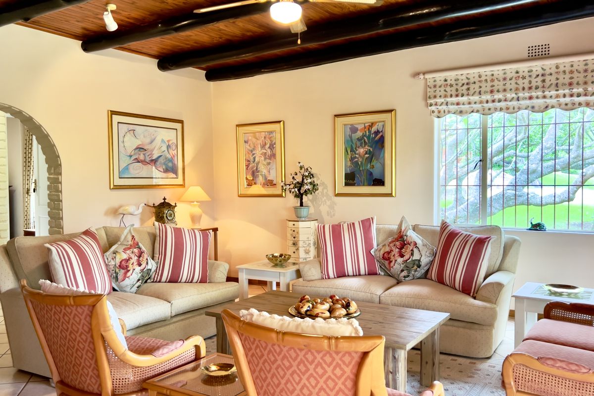 A cozy living room featuring a rustic timber-beamed ceiling, arched doorway, and large windows overlooking the garden.