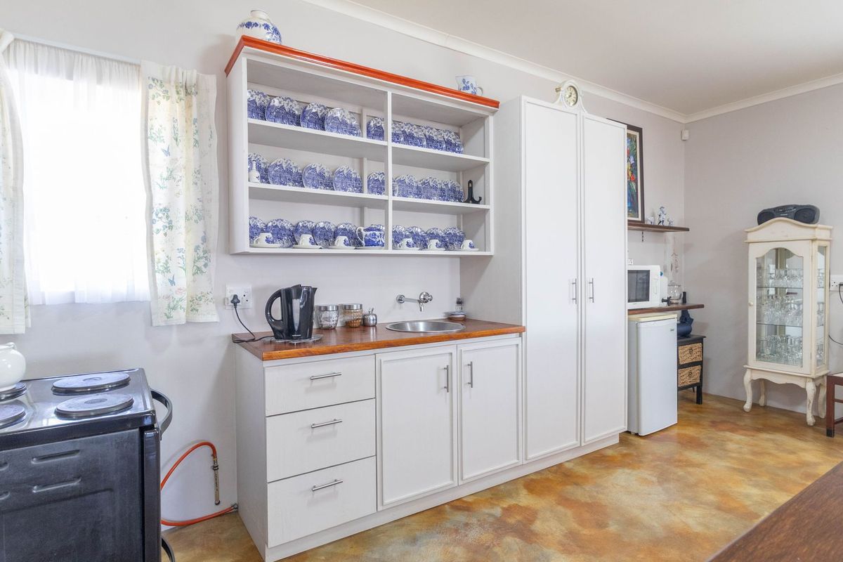 A functional kitchen area featuring white cabinetry, a wooden countertop, a stainless steel sink, and open shelving for display.