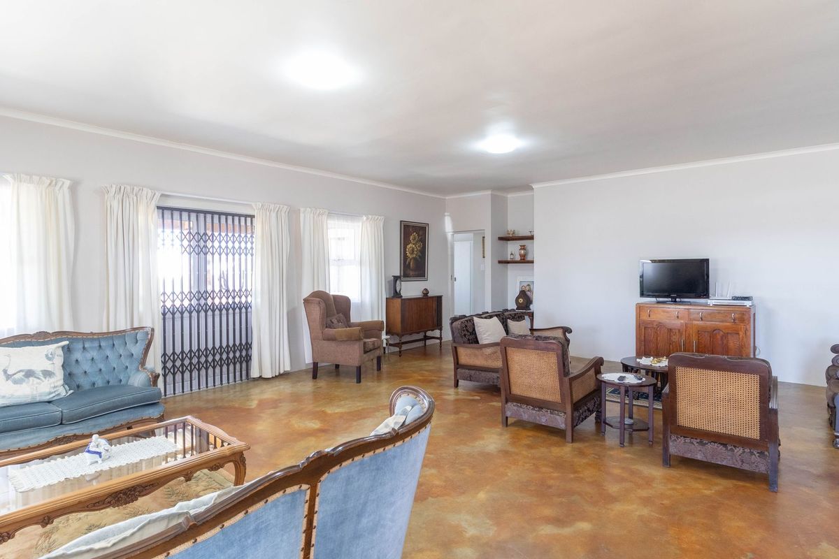 Spacious living room featuring polished concrete floors, large windows with security gates, and built-in wall shelving.