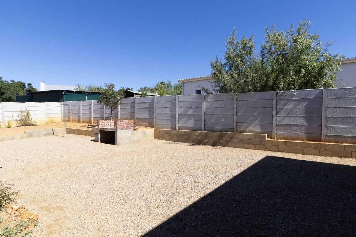 A spacious, low-maintenance rear garden featuring a gravel surface, a built-in brick braai area, and secure precast concrete perimeter walling.