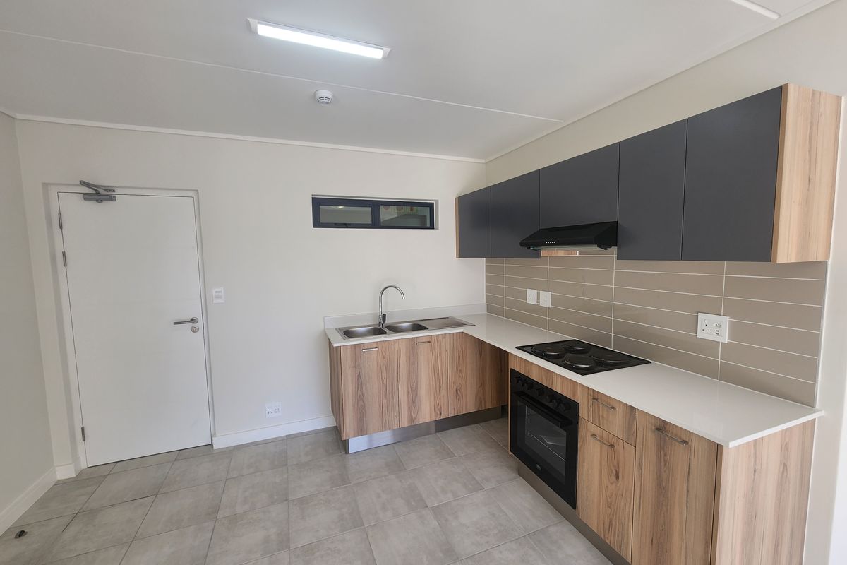 Modern kitchen featuring wood-grain lower cabinets, dark upper cupboards, stone countertops, integrated electric oven, hob, and extractor fan with neutral tiled flooring.