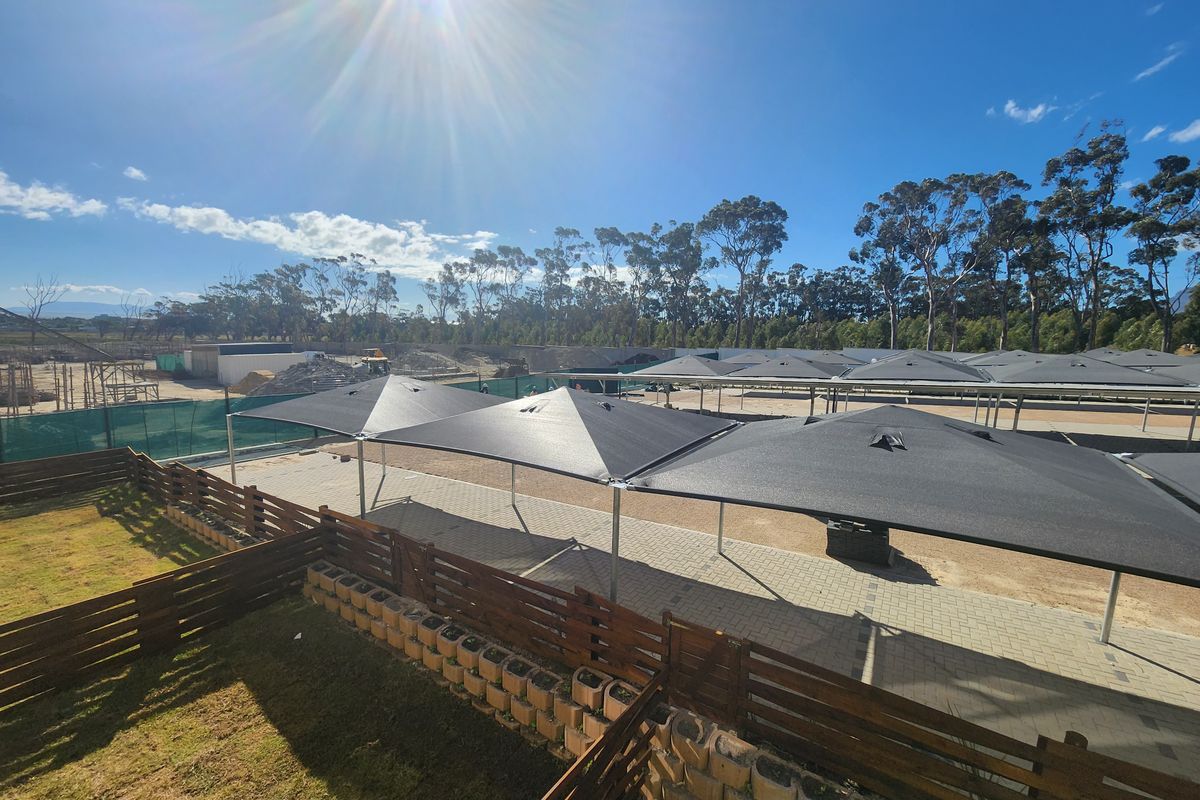 An elevated view of a paved parking area featuring modern shade sail structures, timber fencing, and retaining wall elements in a residential complex setting.