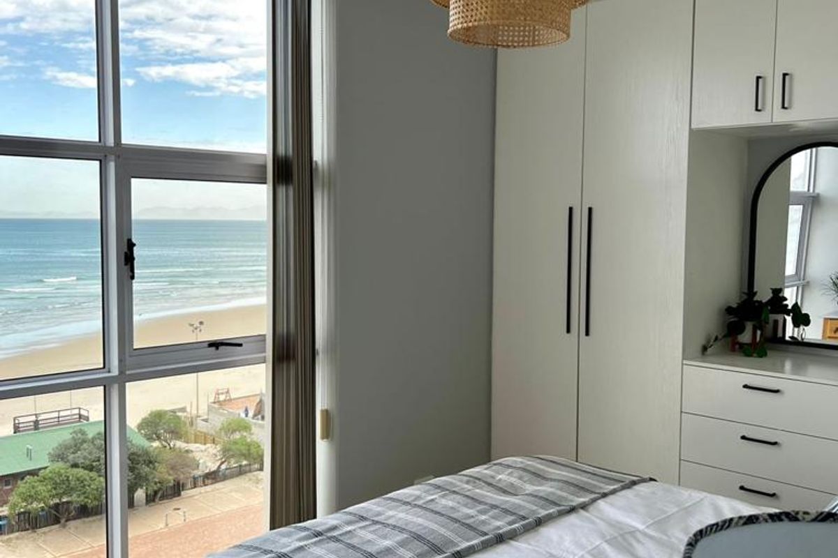 A bright bedroom featuring floor-to-ceiling windows with panoramic ocean views, built-in cabinetry, and modern finishes.
