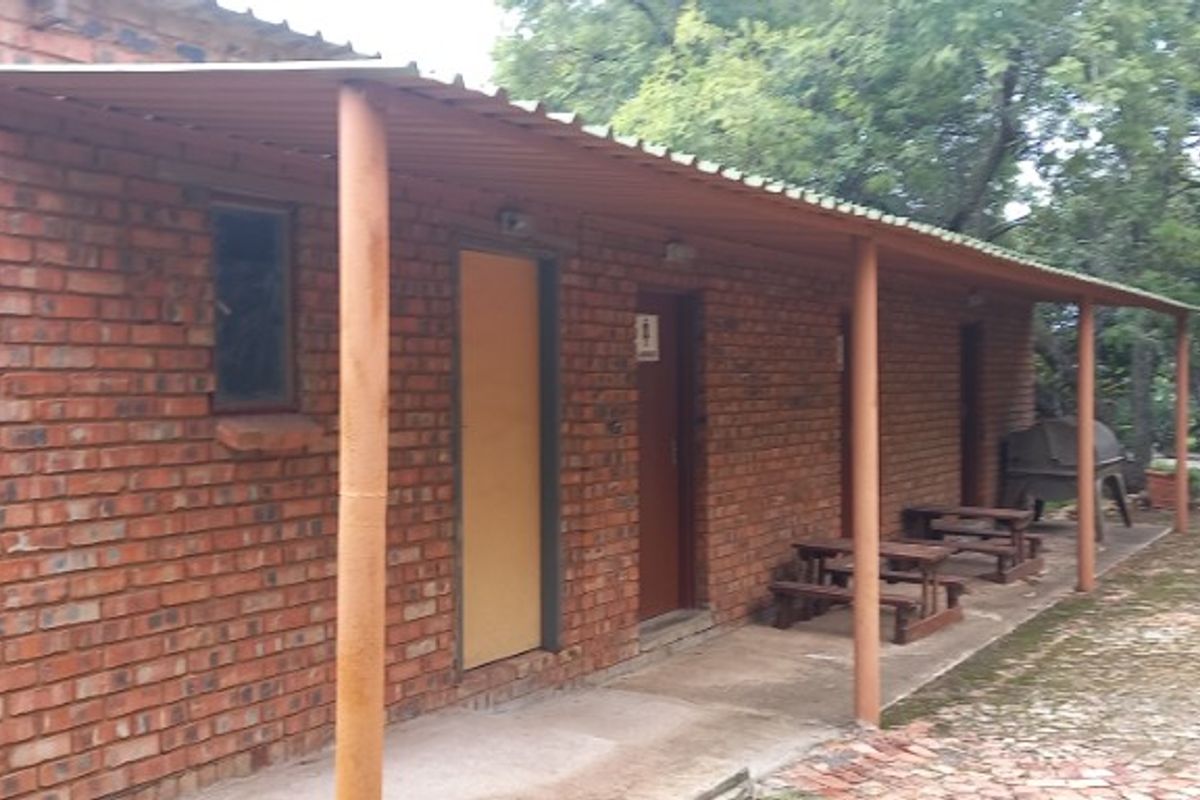 Exterior view of a brick-built utility building featuring a covered walkway and multiple access doors, set within a garden environment.