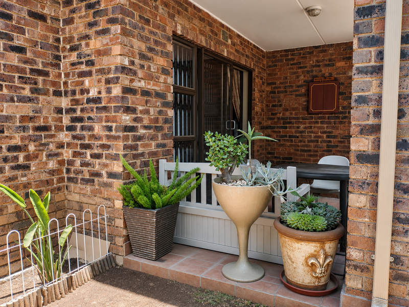 A covered patio area featuring exposed brick walls, tiled flooring, and a sliding glass door with a security gate.