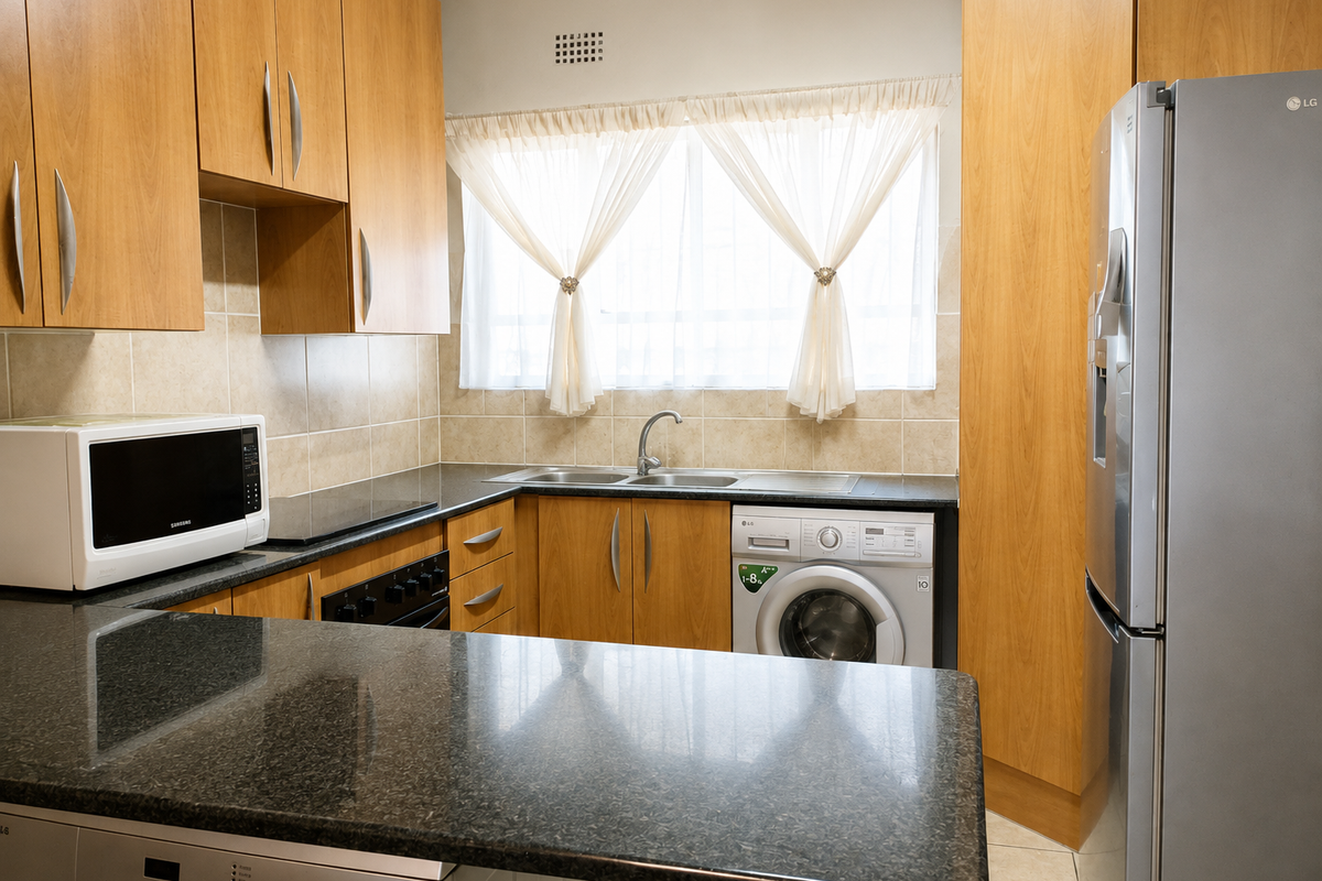 A functional kitchen featuring wood-finish cabinetry, granite countertops, a double sink, and integrated laundry appliances, offering a practical layout for daily use.